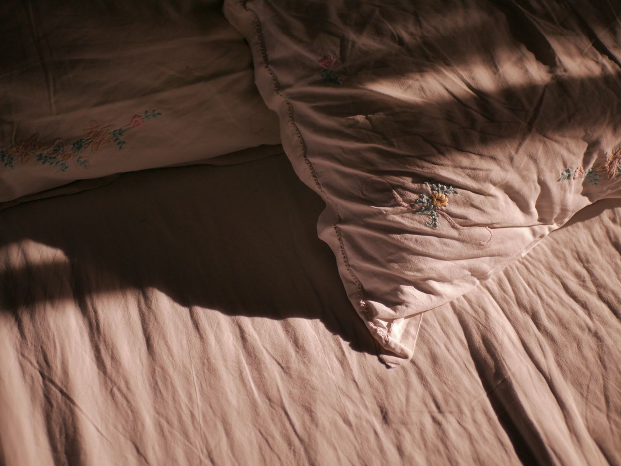 A cozy bedroom scene with soft light highlighting pillows and a bed sheet.