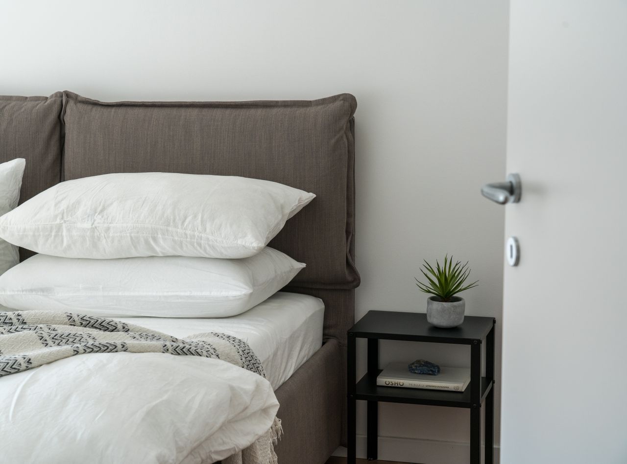 A serene and stylish bedroom featuring a comfortable bed with clean white bedding and a side table with decor.