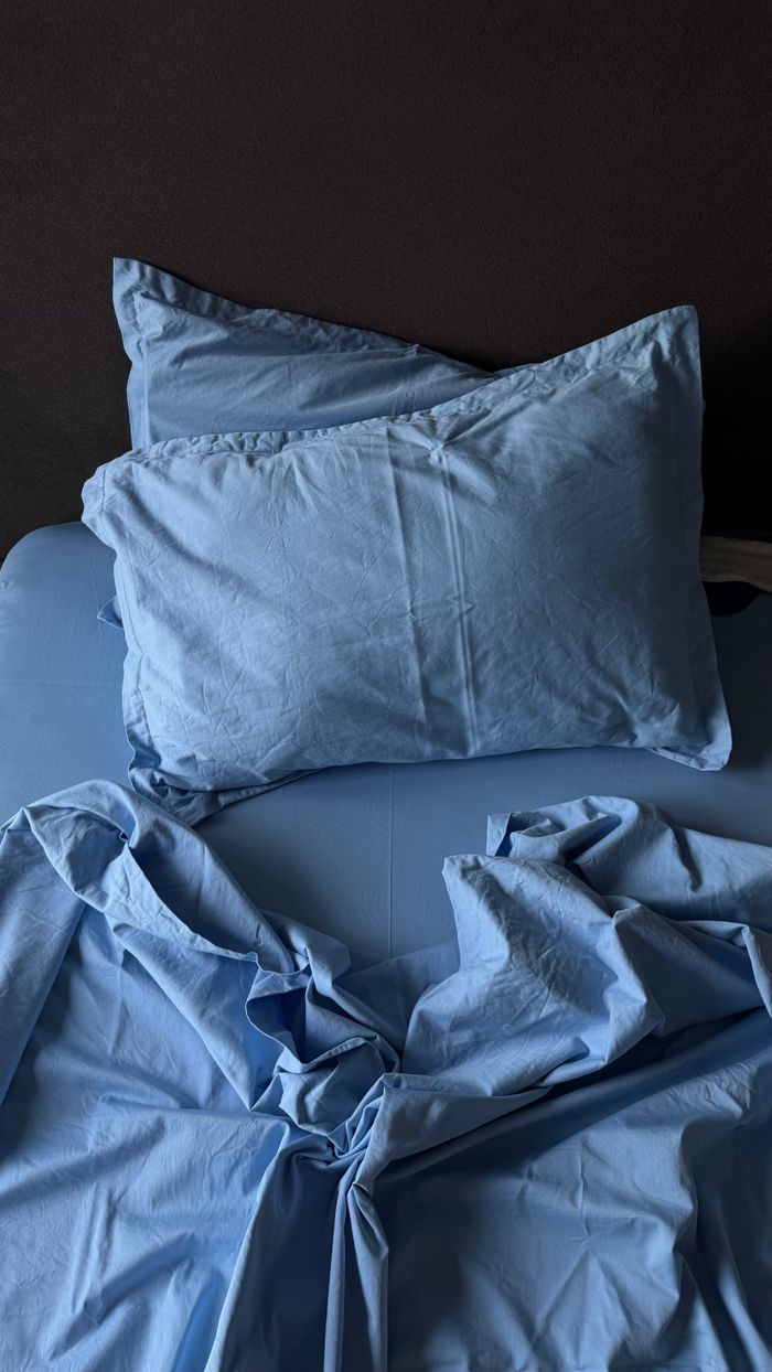 A cozy, serene setting featuring blue bed sheets and a pillow with dramatic lighting.